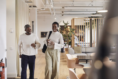 Happy male and female business professionals walking in office corridor