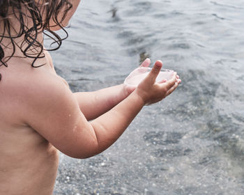 Midsection of shirtless woman hand in sea