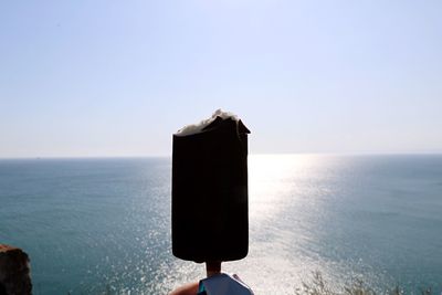 Close-up of hand holding ice cream against sea