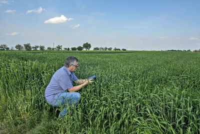 Side view of man using smart phone crouching on field against sky