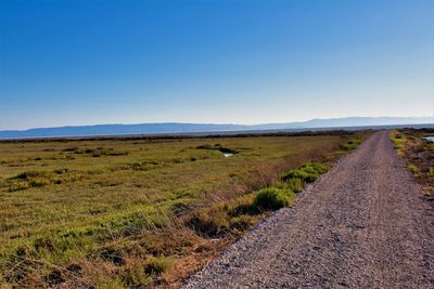 View of dirt road amidst field against clear sky