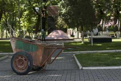 The background out of focus, a janitor is manually sweeping a walkway in a park. 