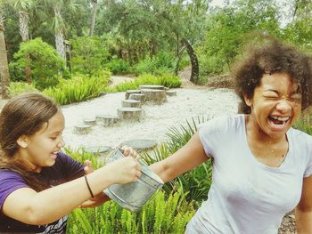 Happy friends smiling by trees against plants