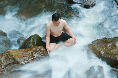 High angle view of man meditating in waterfall