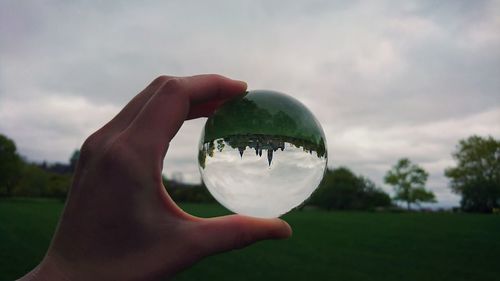 Close-up of hand holding crystal ball against trees