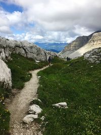 Rear view of man walking on dirt road on mountain against sky