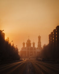 Road amidst buildings against clear sky during sunset