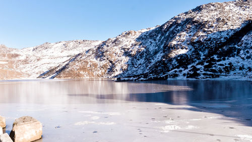 Frozen lake by snowcapped mountain against sky