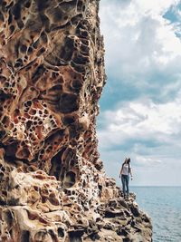 Woman standing on rock formation by sea against sky