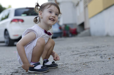 Side view of girl crouching on road against car
