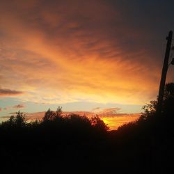 Silhouette trees on landscape against orange sky