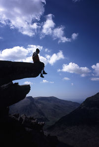 Low angle view of man sitting mountain against sky at snowdonia