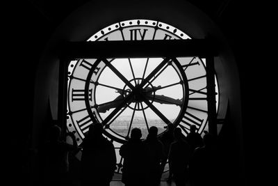 Silhouette people standing against wall clock