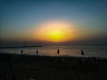 Silhouette people on beach against sky during sunset