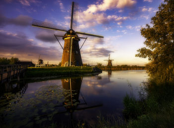 Traditional windmill by lake against sky during sunset