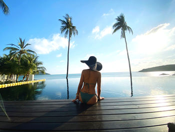 Rear view of woman standing on pier at beach against sky