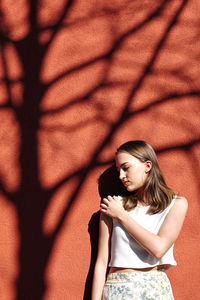 Young woman looking away while standing against wall