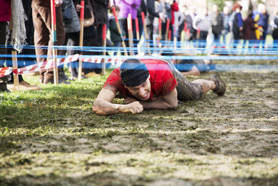 Man crawling under barbed wires on field during race