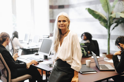 Portrait of confident mature businesswoman leaning on desk in office