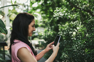 Beautiful agricultural engineer taking a picture of the plants in the greenhousegreen flora inside the rainforest greenhouse