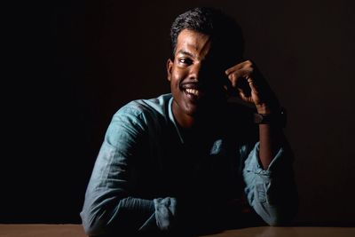 Portrait of smiling mid adult man sitting at table in darkroom