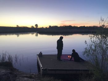 Silhouette man sitting on lake against sky during sunset