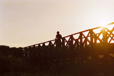 Low angle view of silhouette man standing on bridge against clear sky