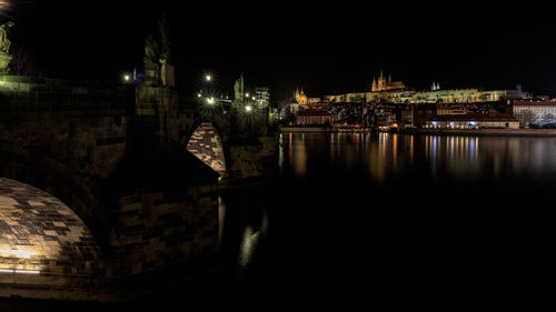 Illuminated buildings by river against sky at night