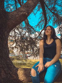 Portrait of young woman sitting on tree trunk