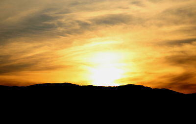 Silhouette landscape against dramatic sky during sunset