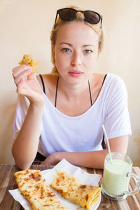 Portrait of young woman with drink sitting on table