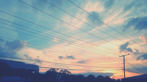 Low angle view of electricity pylon against cloudy sky