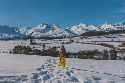 A full-body shot of a young caucasian woman walking towards the camera in the french alps mountains