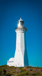 Low angle view of lighthouse on field against clear blue sky