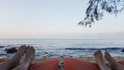 Low section of people relaxing by sea against sky