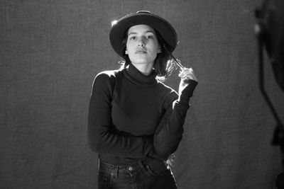 Portrait of woman wearing hat standing against backdrop