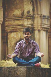 Young man meditating against temple