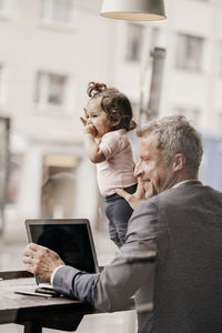 Businessman with little daughter working on laptop in cafe