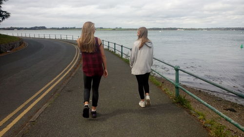 Rear view of people walking on road by sea against sky