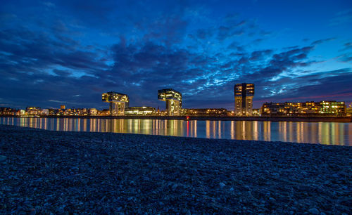 Illuminated buildings by sea against sky at night