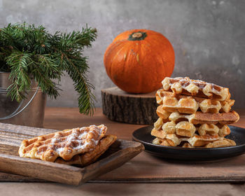 Homemade waffles with sugar bubble and orange pumpkin on a wooden tray