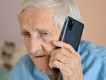 Happy elderly 90-year-old woman with glasses wearing a blue jacket smiles using a smartphone.