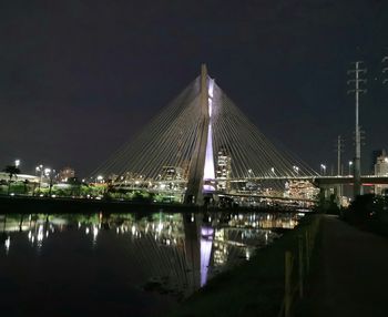 Illuminated bridge over river against sky at night