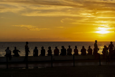 Silhouette people on beach against sky during sunset