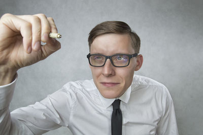 Portrait of man holding eyeglasses against gray background