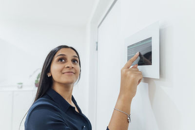 Smiling woman using smart home device on wall