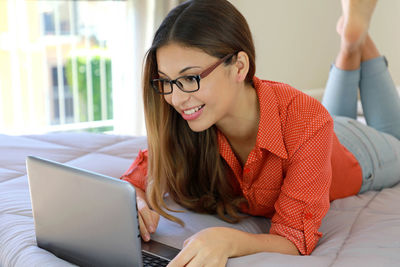 Young woman using laptop while lying on bed