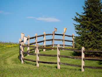 Fence on grassy field against blue sky