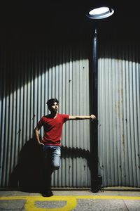 Young man leaning on street light while standing against corrugated sheet