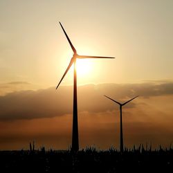 Silhouette windmills on land against sky during sunset